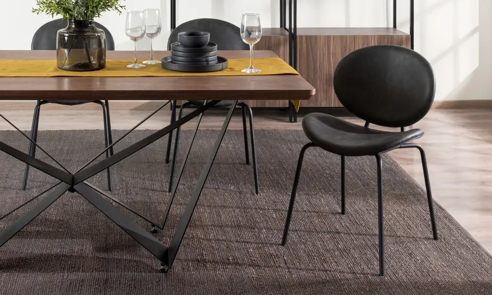 Salle à manger moderne avec mobilier de style industriel, avec une table en bois rectangulaire avec des pieds en métal noir géométrique, des chaises en cuir noir, des étagères minimalistes et des accents décoratifs chauds.