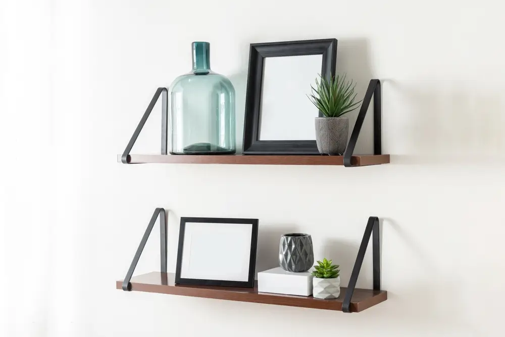 Composition inspirée de la Scandinavie avec deux étagères flottantes en bois avec des consoles en métal noir, décorées de tableaux encadrés, bouteille en verre vert, mini succulents et vases en céramique sur mur blanc.