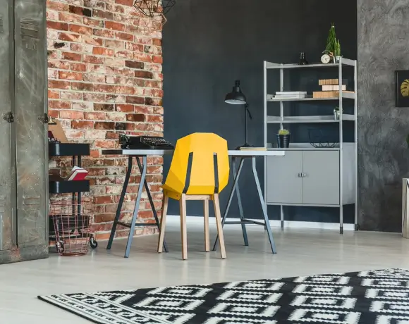 Intérieur loft avec mur en briques, bureau, chaise jaune et bibliothèque.