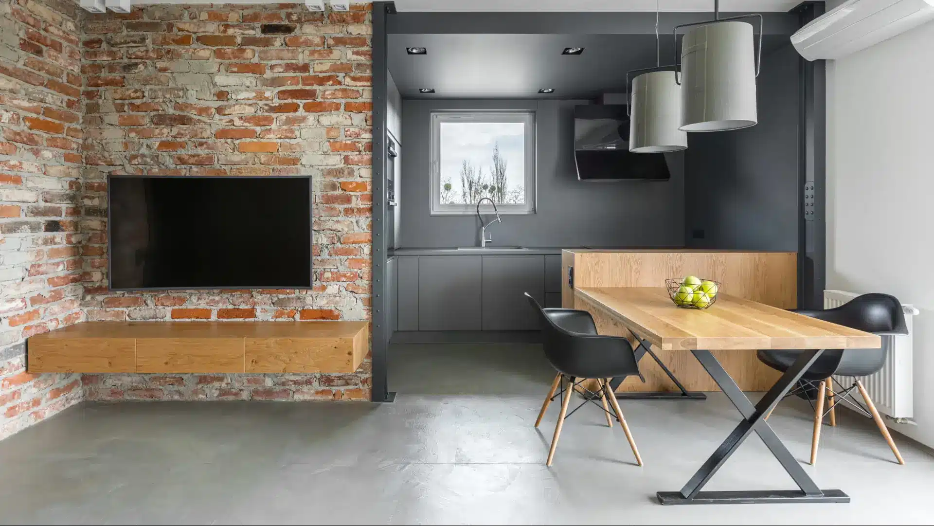 Intérieur de style industriel avec kitchenette, télévision, table, chaises et mur en brique.